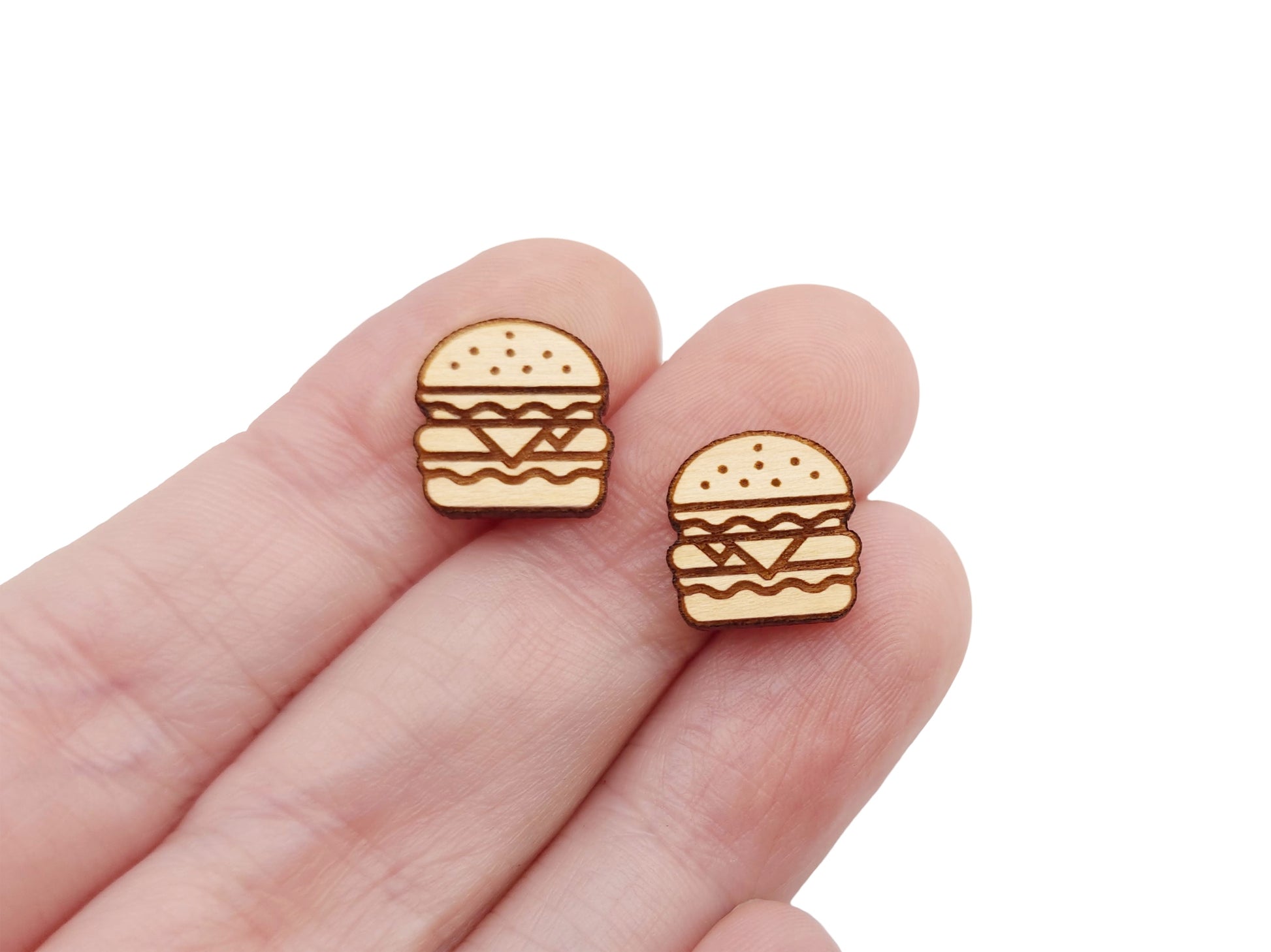 a hand holding a pair of wooden cabochon stud earring blanks cut and engraved to look like a cheeseburger