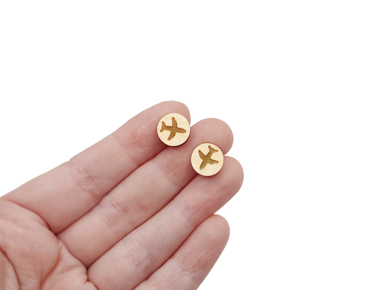 a hand holding a pair of round wooden cabochon earring blanks engraved with a airplane silhouette