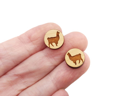 a hand holding a pair of round wooden cabochon earring blanks engraved with a llama silhouette