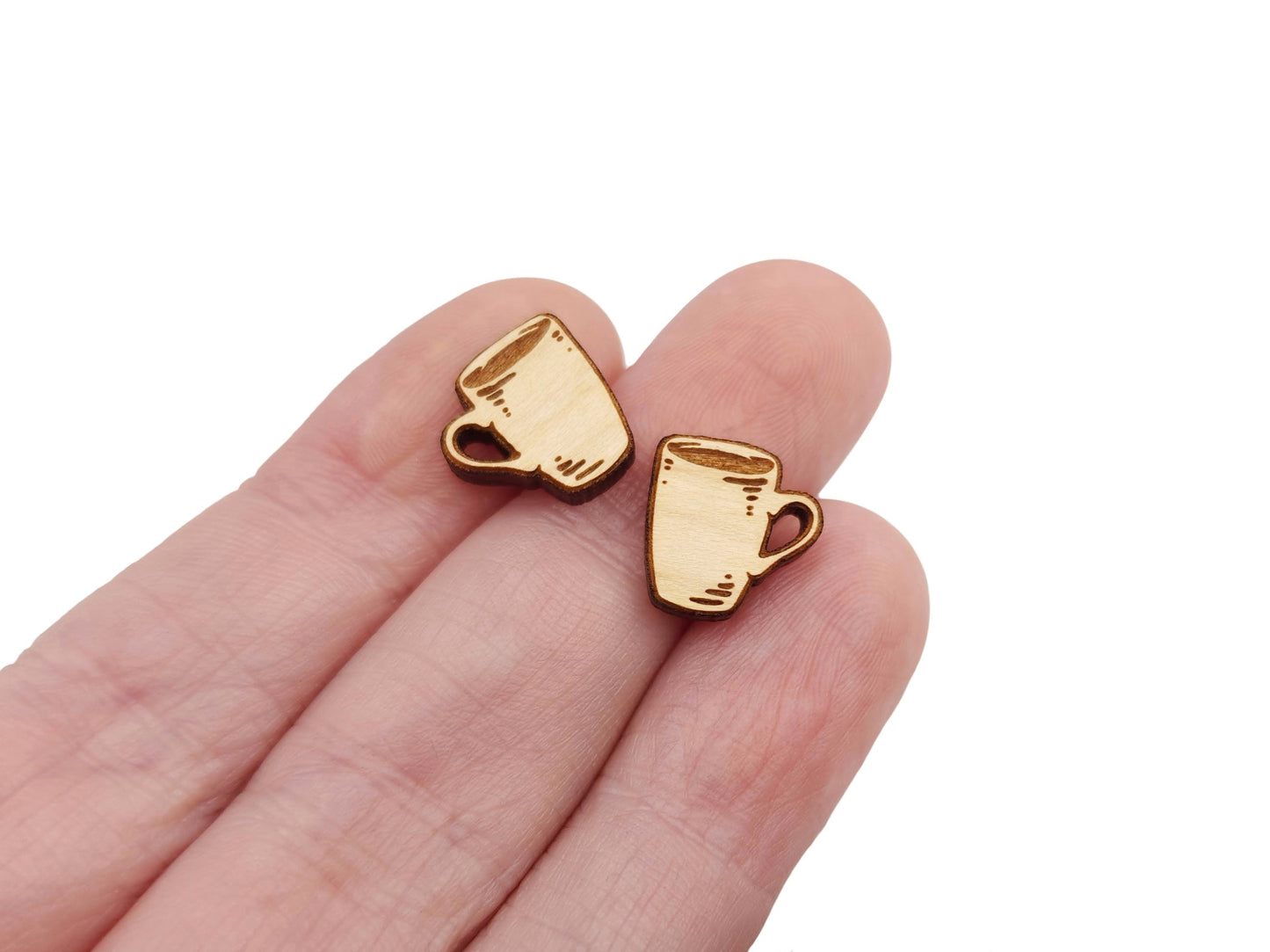 a hand holding a pair of wooden cabochon earring blanks cut and engraved to look like a coffee mug