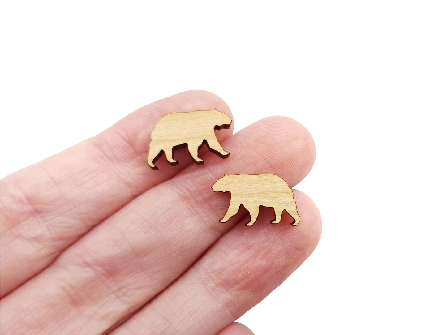 A hand holding a pair of wood and acrylic cabochon earring blanks cut in the shape of a bear