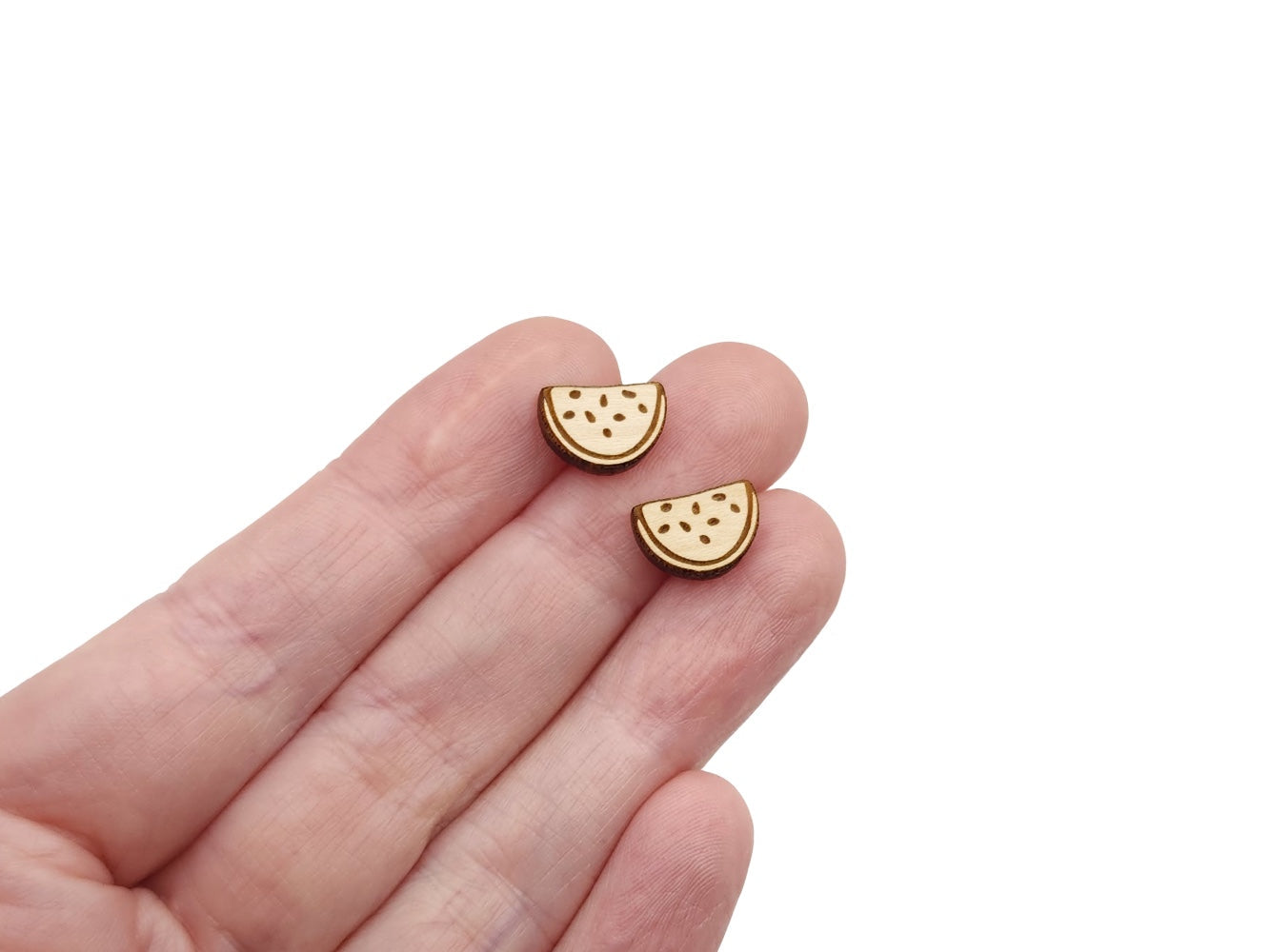 a hand holding a pair of wooden cabochon earring blanks cut and engraved to look like a watermelon