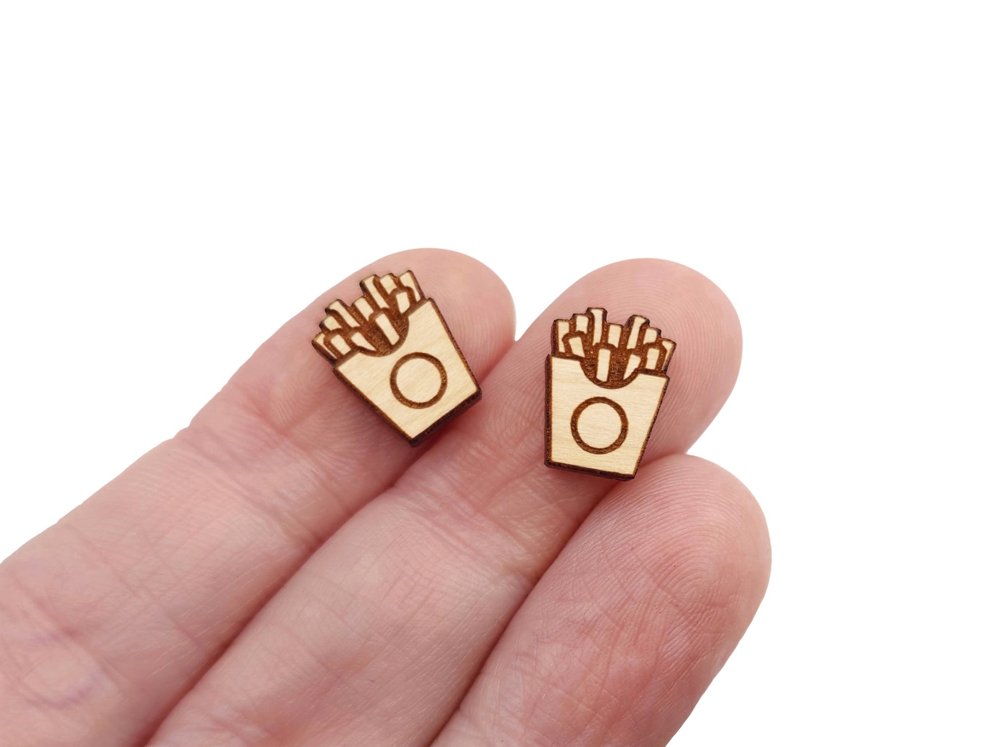 a hand holding a pair of wooden cabochon stud earring blanks cut and engraved to look like french fries