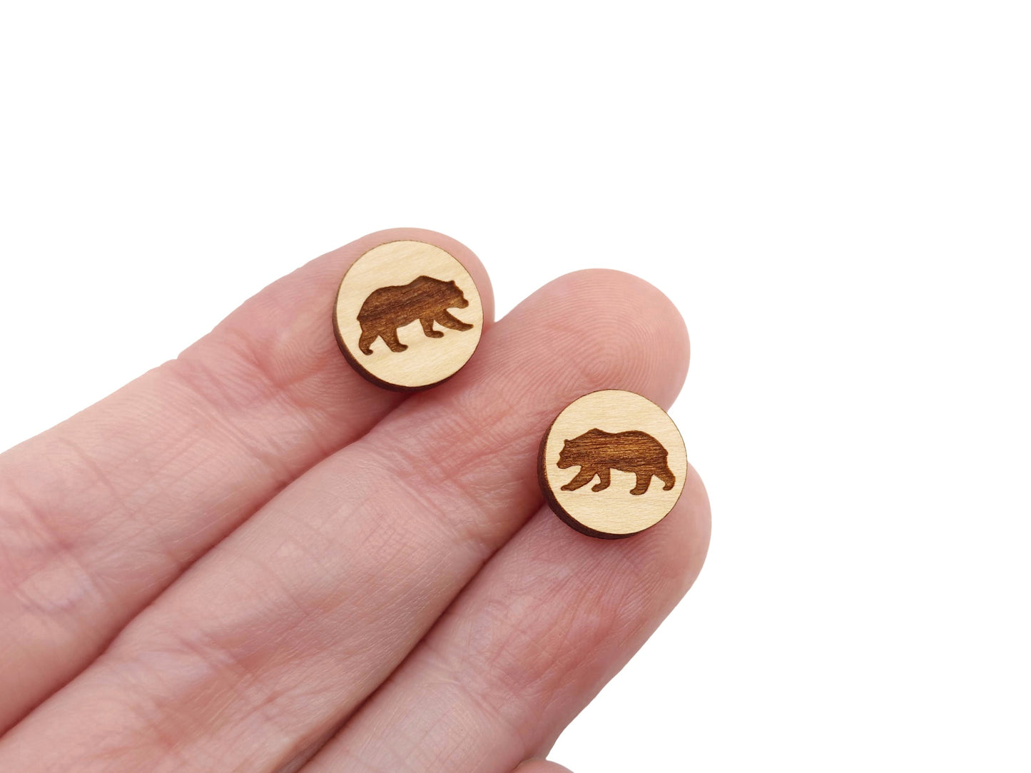 a hand holding a pair of round wooden cabochon earring blanks engraved with a bear silhouette