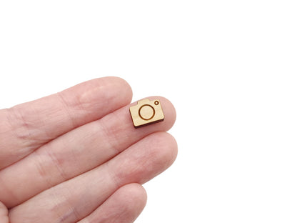 a person's hand holding a pair of wooden cabochon stud earring blanks cut and engraved to look like a camera