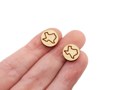 a person's hand holding a pair of round wooden cabochon earring blanks engraved with the outline of Texas