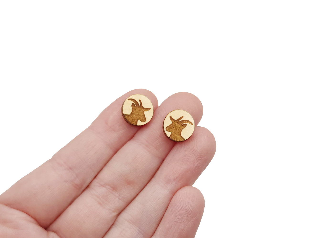 a hand holding a pair of round wooden cabochon earring blanks engraved with a goat silhouette