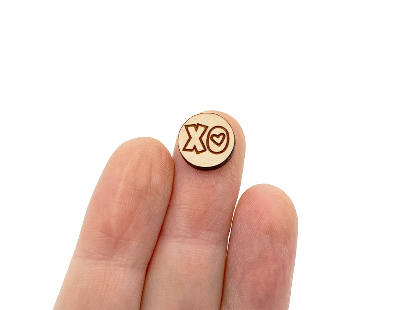 a hand holding a round wooden cabochon earring blanks engraved with an XO Heart design