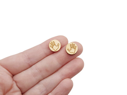 a person's hand holding a pair of round wooden cabochon earring blanks engraved with a handprint outline