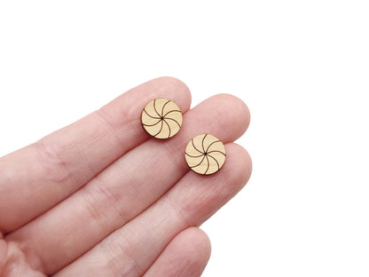 a hand holding a pair of wooden cabochon stud earring blanks cut and engraved to look like peppermint candies