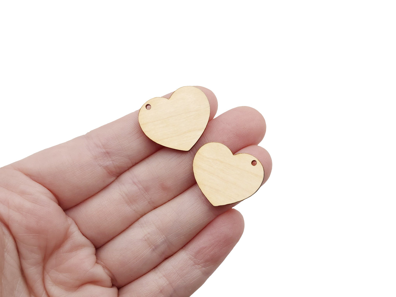 a hand holding a pair of heart-shaped wood or acrylic jewelry charm blanks