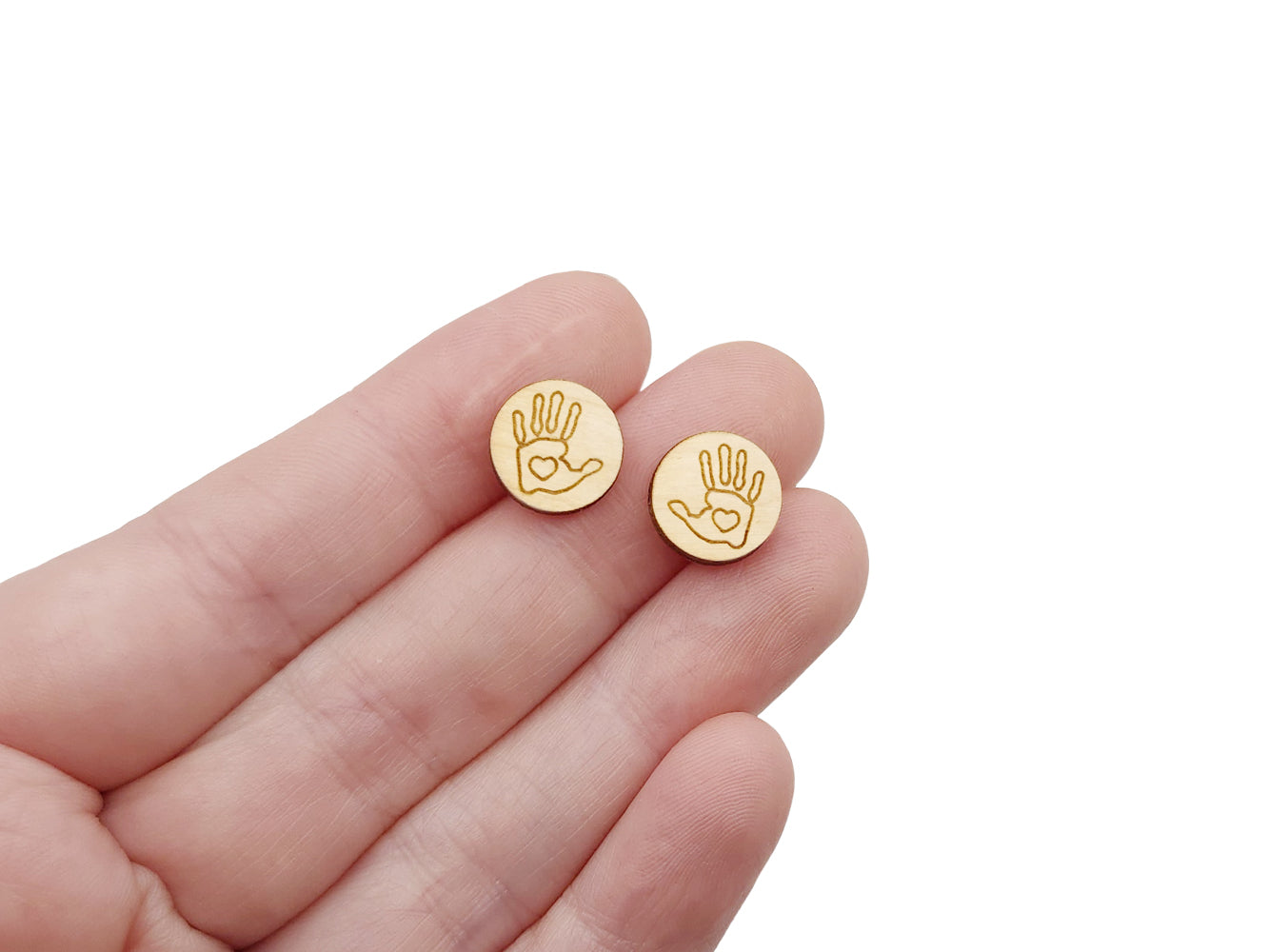 a hand holding a pair of round wooden cabochon earring blanks engraved with a handprint outline with a heart