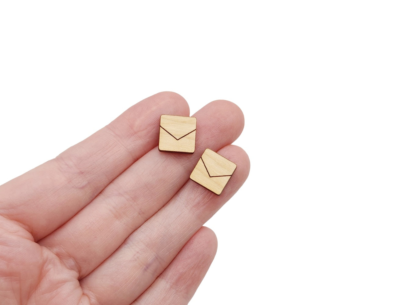 a hand holding a pair of wooden cabochon stud earring blanks cut in a square shape and engraved with a chevron line