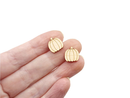 a hand holding a pair of wooden cabochon stud earring blanks cut and engraved to look like pumpkins