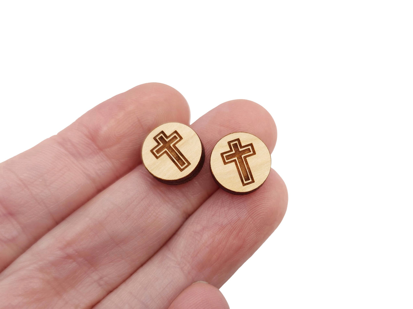 a hand holding a pair of round wooden cabochon earring blanks engraved with a cross