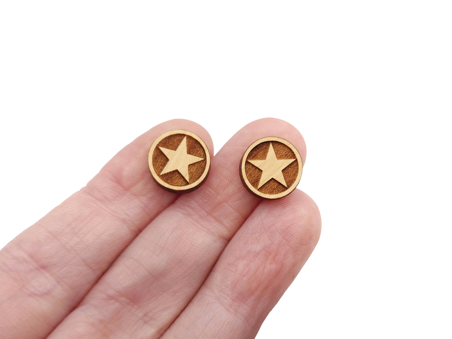 a hand holding a pair of round wooden cabochon earring blanks engraved with a framed star