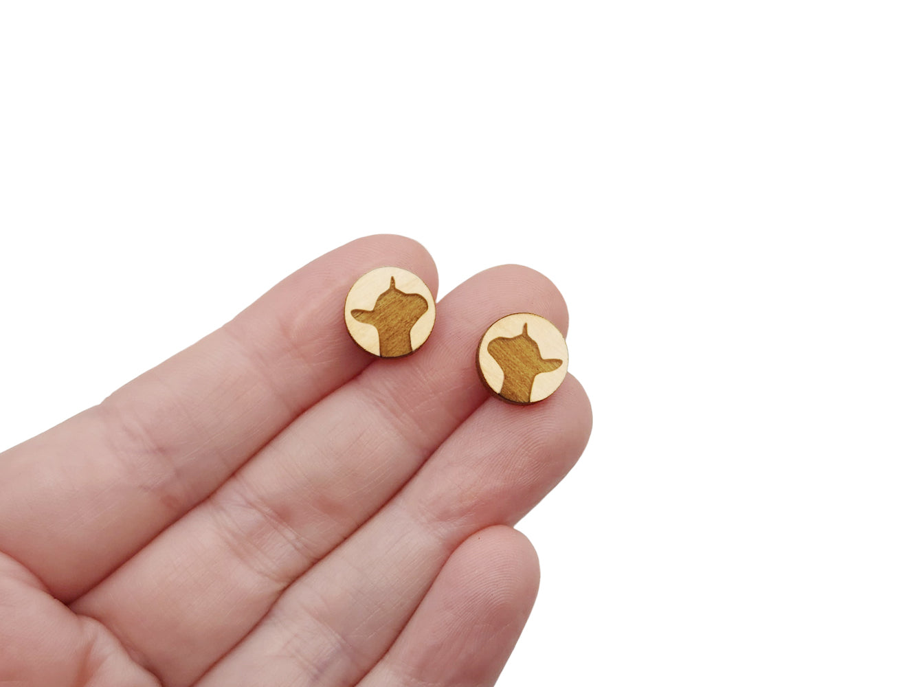 a hand holding a pair of round wooden cabochon earring blanks engraved with a dairy goat silhouette