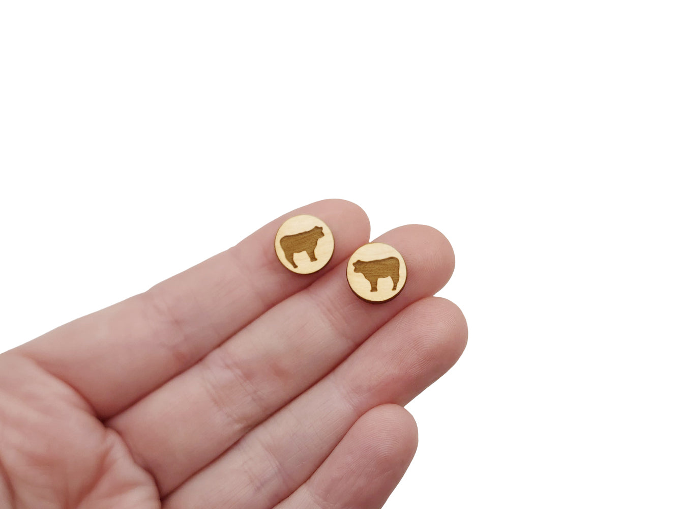 a hand holding a pair of round wooden cabochon earring blanks engraved with a cow silhouette