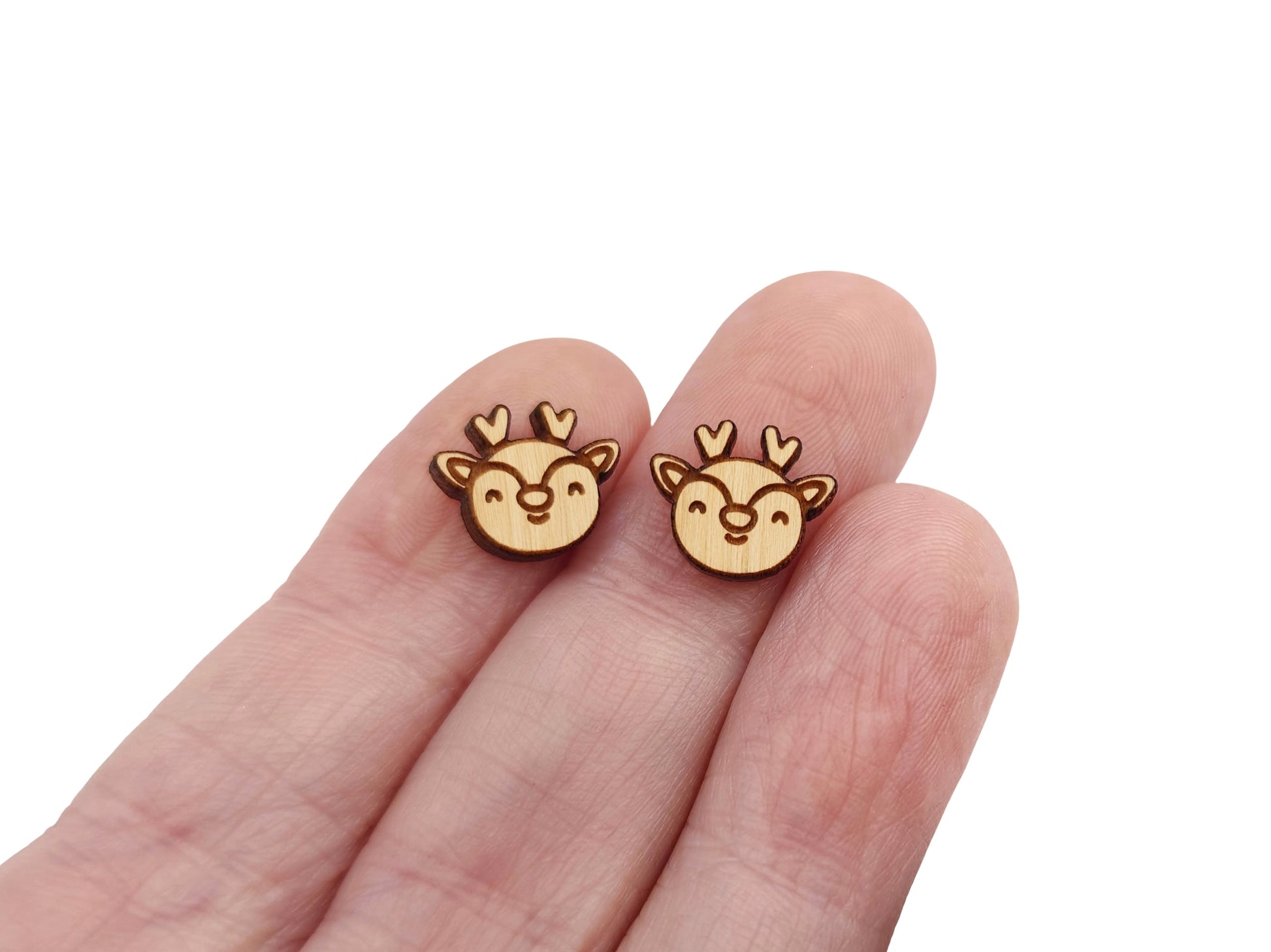 a hand holding a pair of wooden cabochon stud earring blanks cut and engraved to look like a reindeer