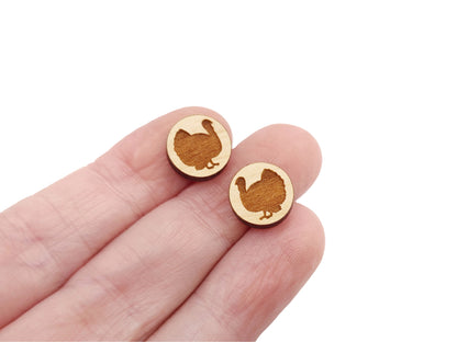 a hand holding a pair of round wooden cabochon earring blanks engraved with a turkey silhouette