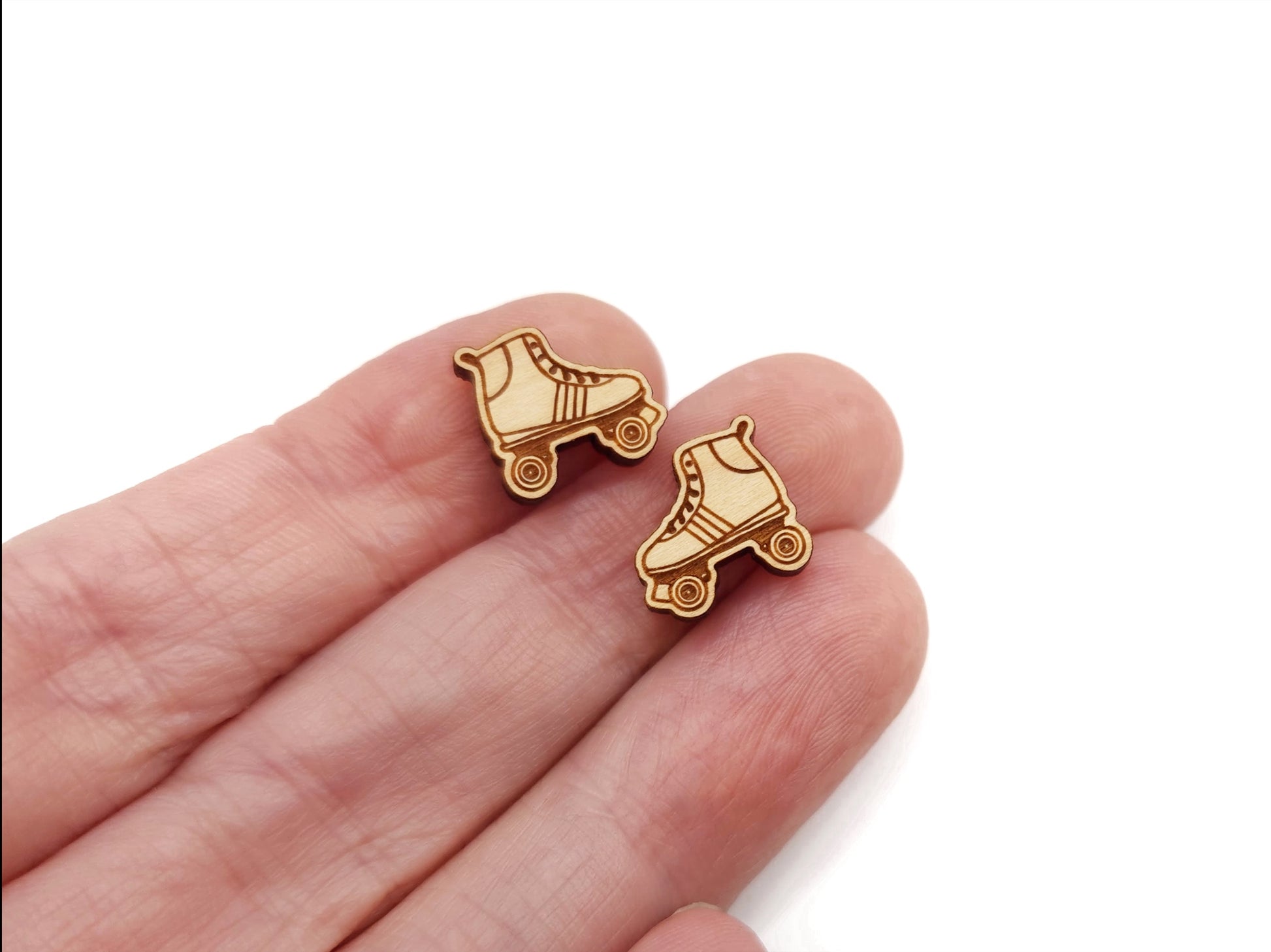 A hand holding a pair of wooden cabochon earring blanks cut and engraved to look like a roller skate