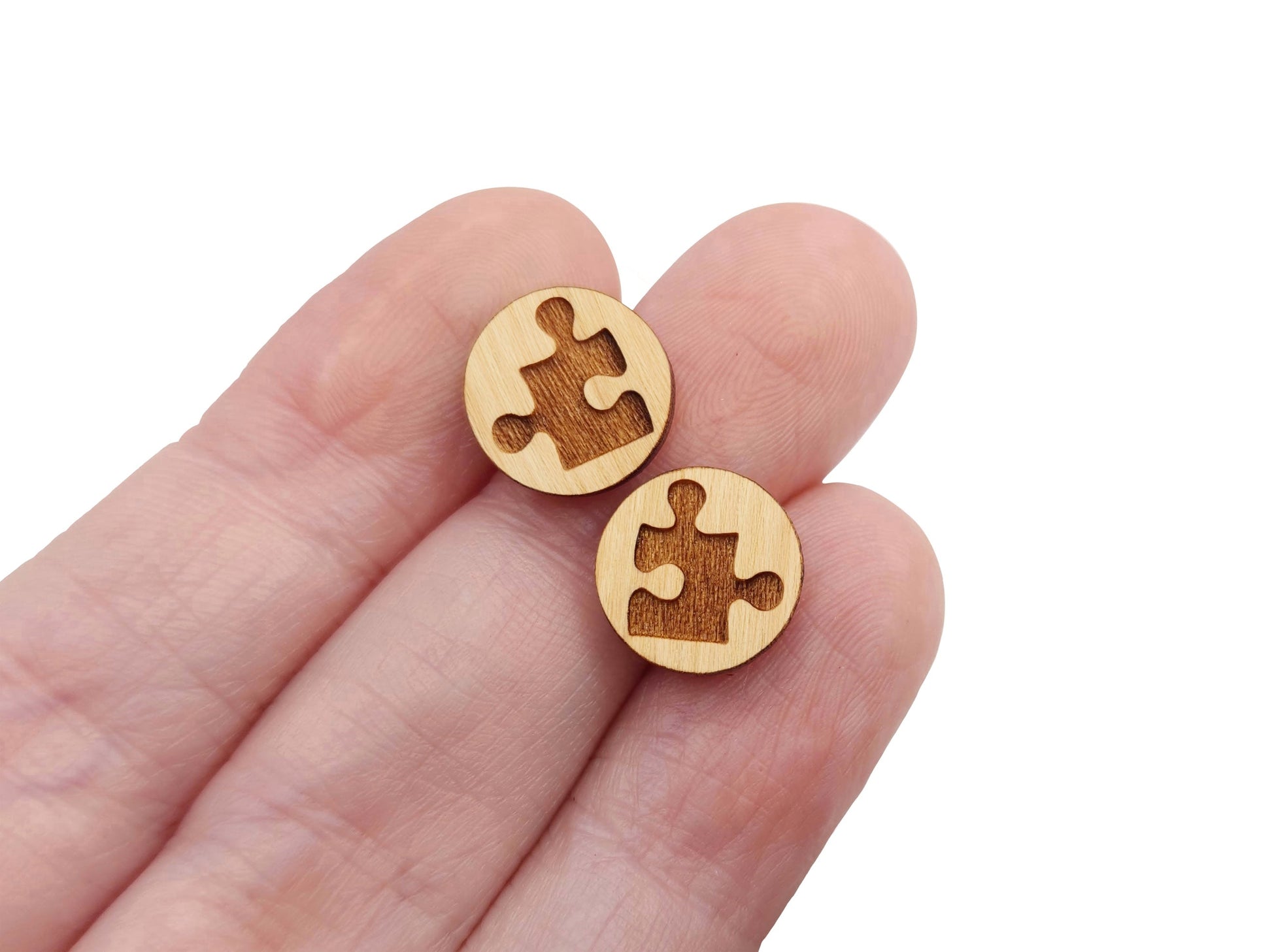 a pair of round wooden cabochon earring blanks engraved with a puzzle piece on a person's hand