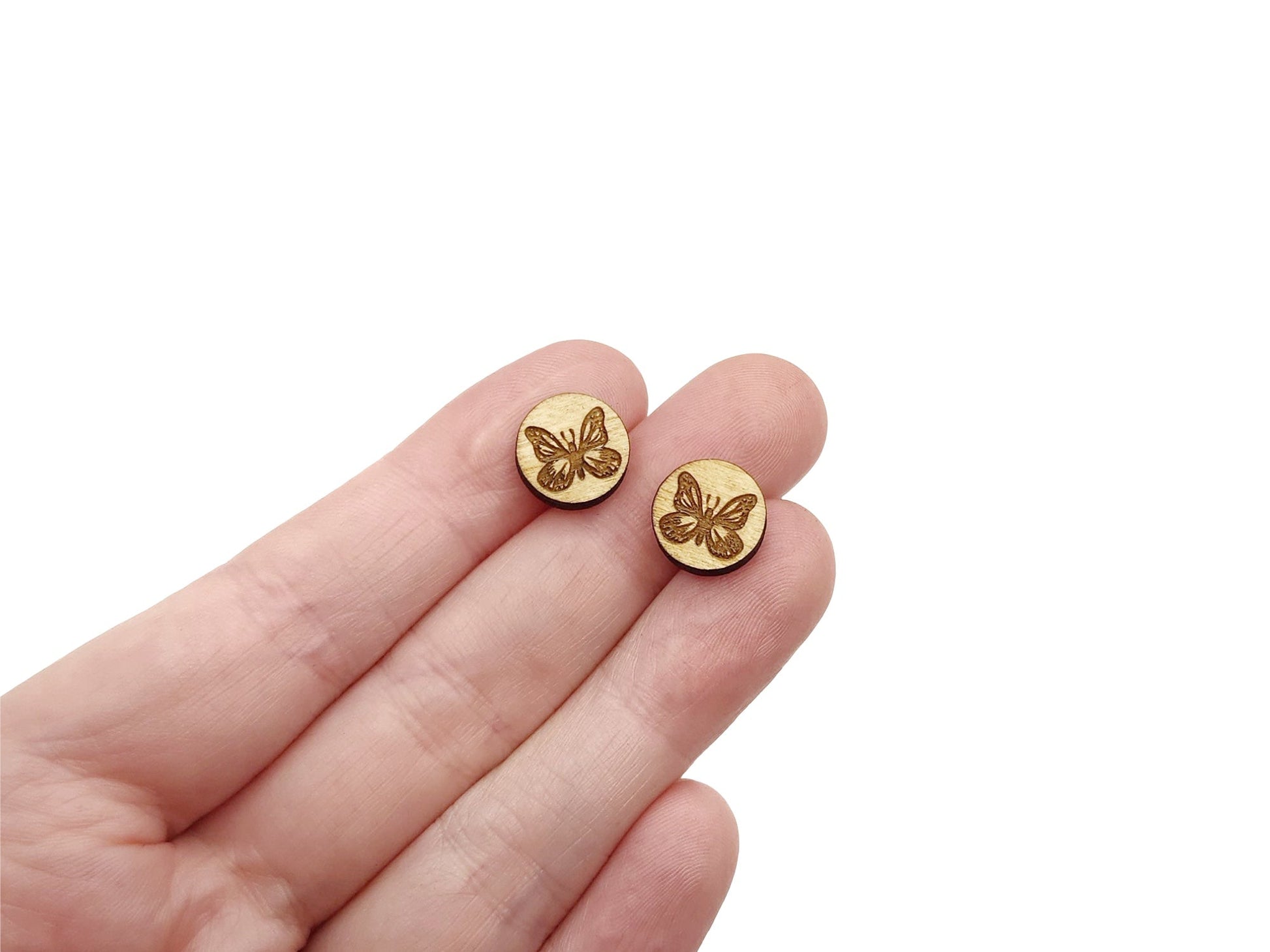 a hand holding a pair of round wooden cabochon stud earring blanks engraved with a butterfly