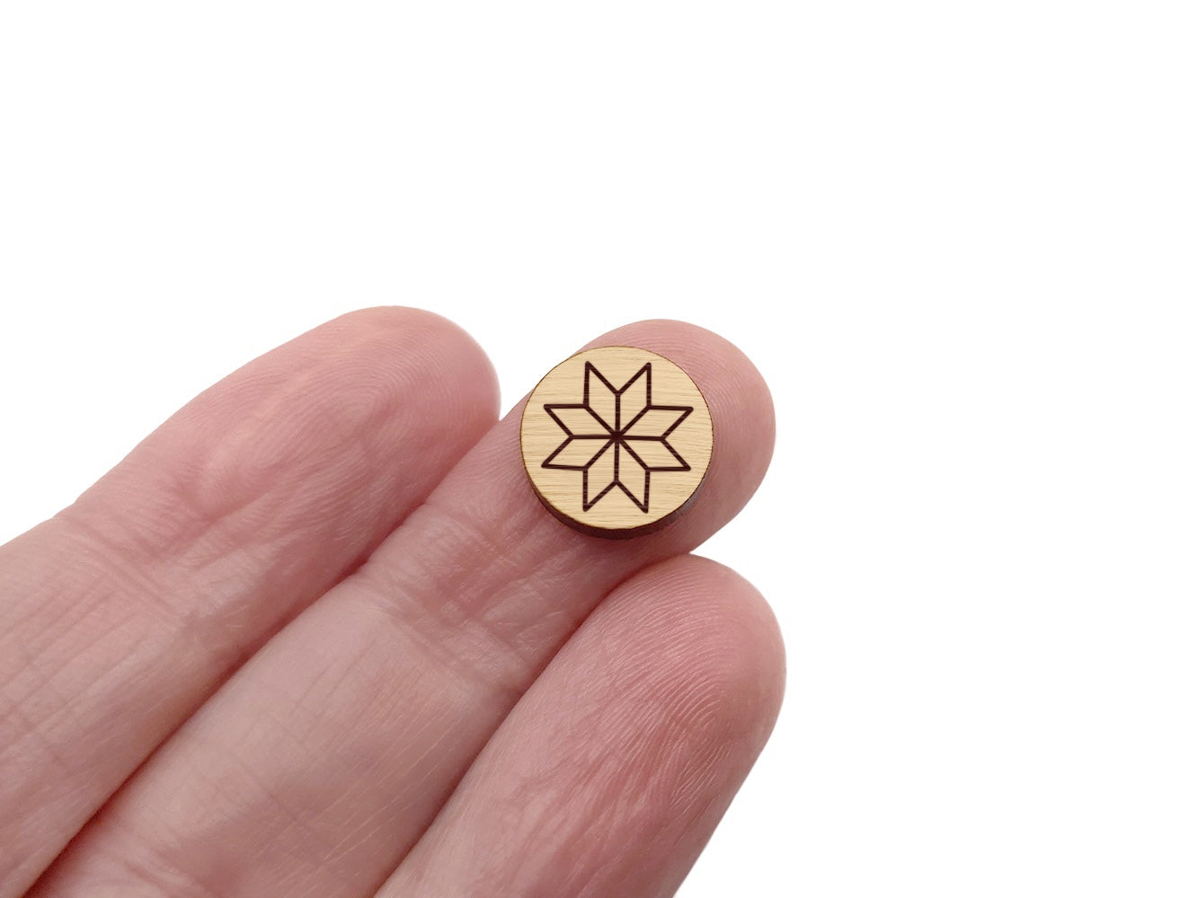 a hand holding a round wooden cabochon stud earring blank engraved with a quilted star design