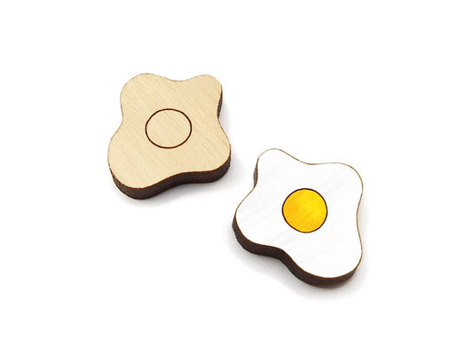 a pair of wooden cabochon stud earring blanks cut and engraved to look like fried eggs, one is painted