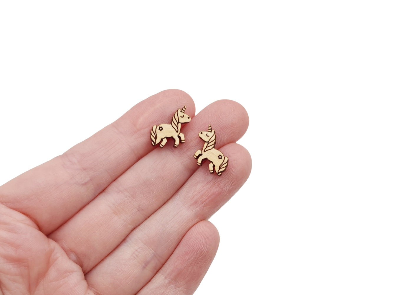 a hand holding a pair of wooden cabochon stud earring blanks cut and engraved to look like a unicorn