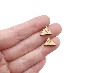 a hand holding a pair of wooden cabochon stud earring blanks cut and engraved to look like snow-capped mountains