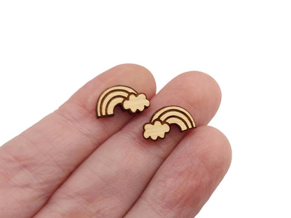 a hand holding a pair of round wooden cabochon earring blanks cut and engraved to look like a rainbow & cloud