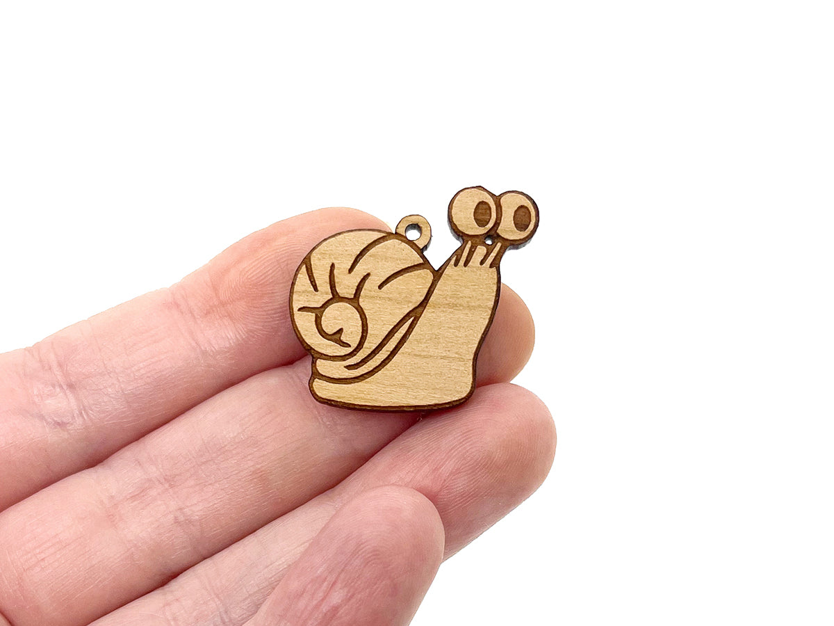 a hand holding a pair of wooden earring blanks cut and engraved to look like a snail