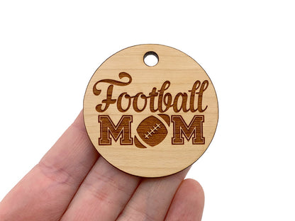 a hand holding a wooden ornament that says football mom