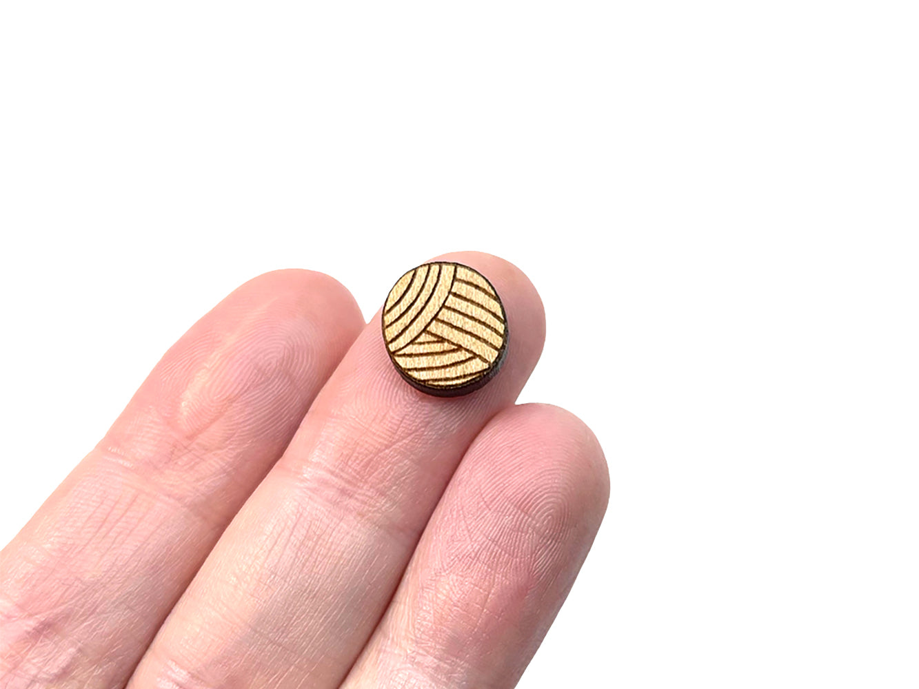 a person's hand holding a pair of wooden cabochon stud earring blanks cut and engraved to look like a ball of yarn