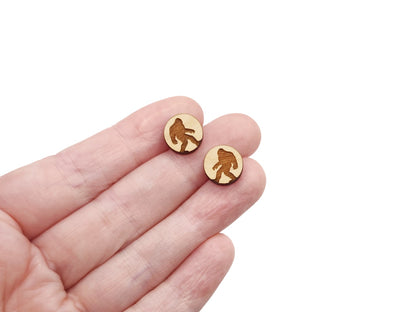 a hand holding a pair of round wooden cabochon earring blanks engraved with a Bigfoot