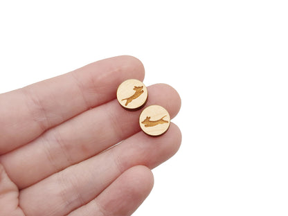 a hand holding a pair of round wooden cabochon earring blanks engraved with a leaping dachshund