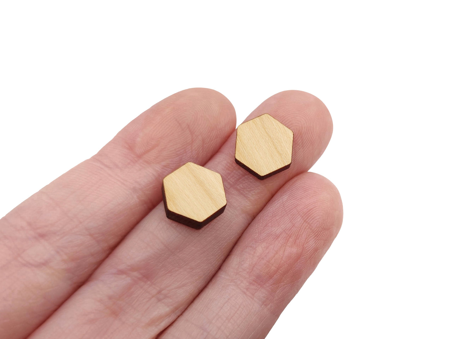 A hand holding a pair of wood and acrylic cabochon earring blanks cut in the shape of a hexagon