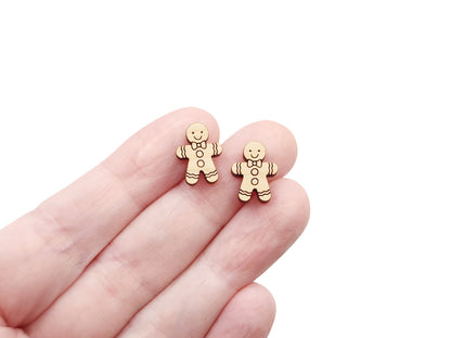 a hand holding a pair of wooden cabochon stud earring blanks cut and engraved to look like a gingerbread man