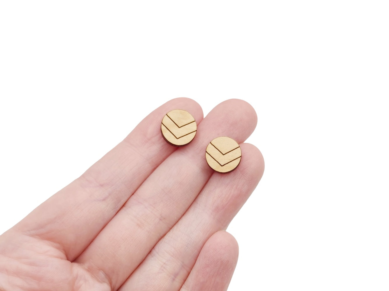 a hand holding a pair of round wooden cabochon earring blanks engraved with chevron lines