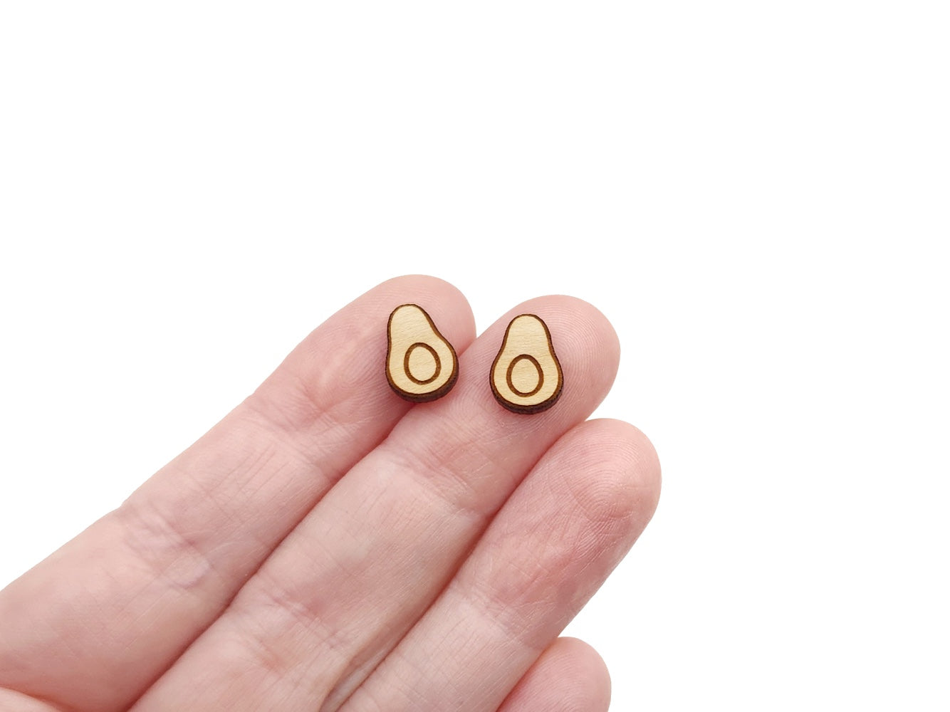 a hand holding a pair of wooden cabochon stud earring blanks cut and engraved to look like an avocado