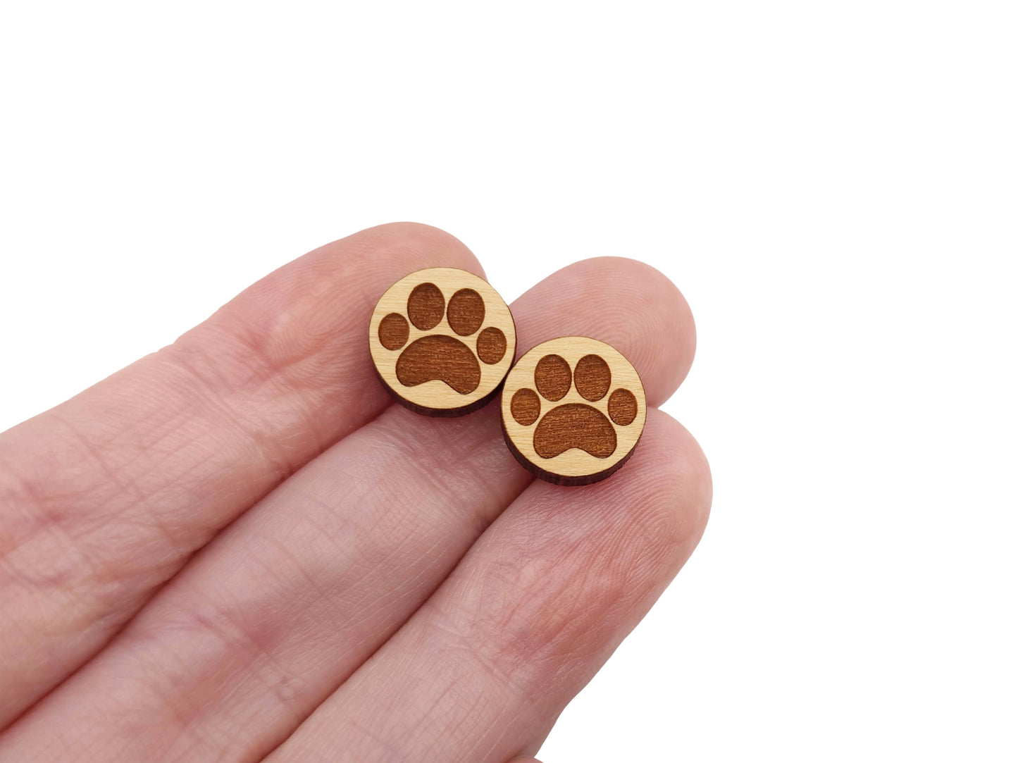 a hand holding a pair of round wooden cabochon earring blanks engraved with a paw print