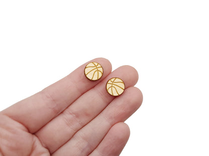 a person holding a pair of wooden cabochon stud earring blanks cut and engraved to look like a basketball