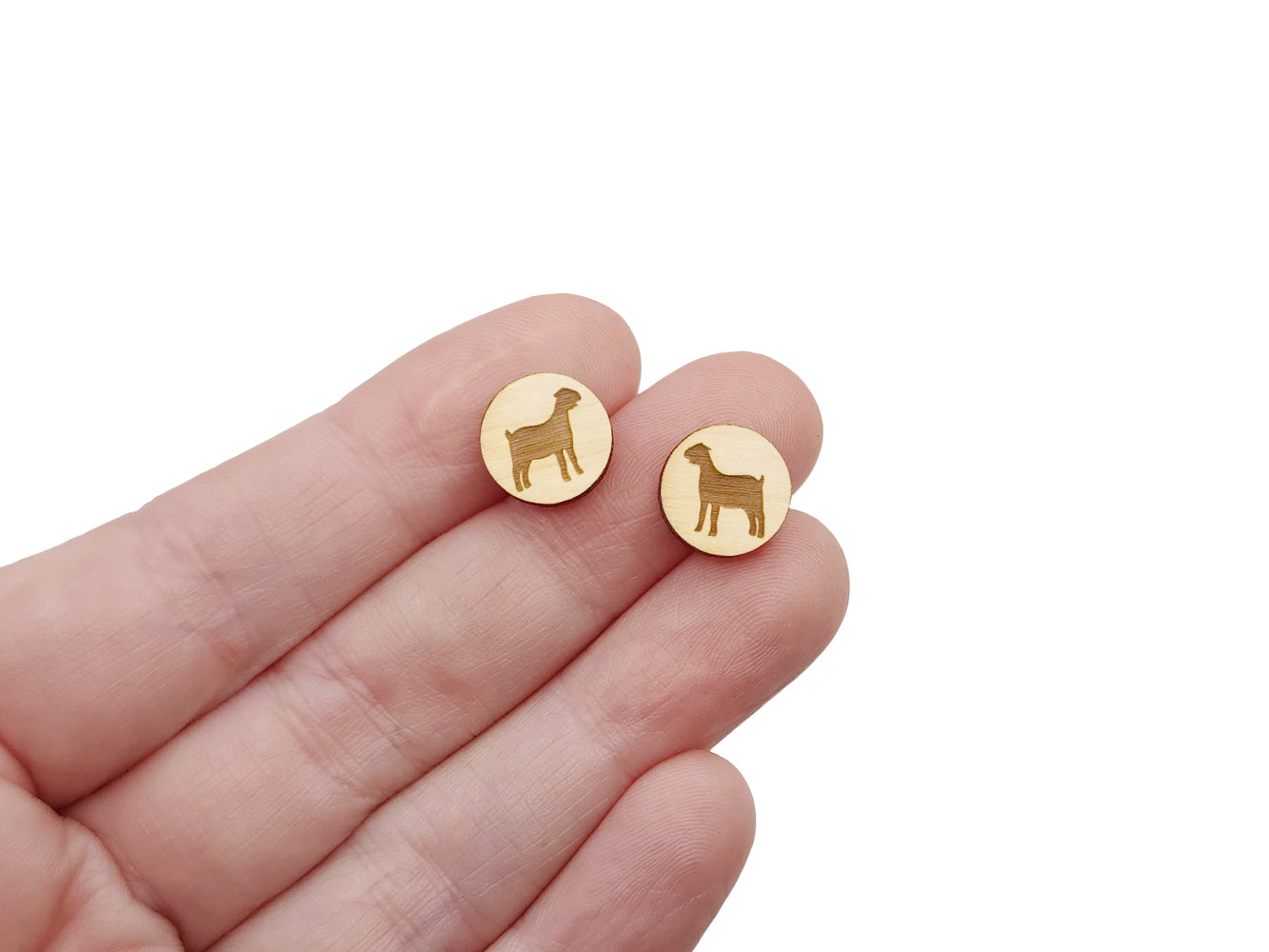 a hand holding a pair of round wooden cabochon earring blanks engraved with a nubian goat silhouette