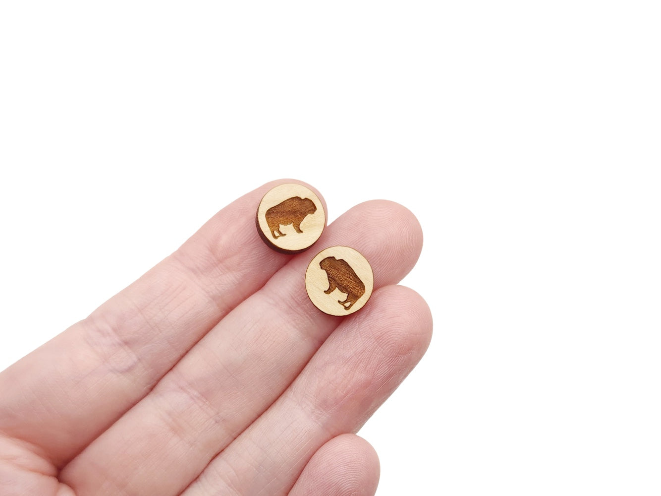 a hand holding a pair of round wooden cabochon earring blanks engraved with a buffalo silhouette design