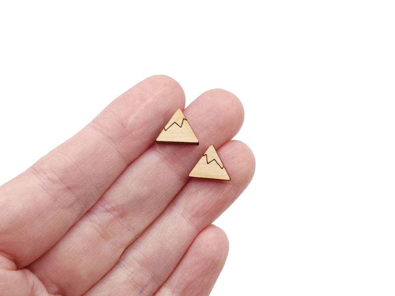 a hand holding a pair of wooden cabochon stud earring blanks cut and engraved to look like a snow-capped mountain