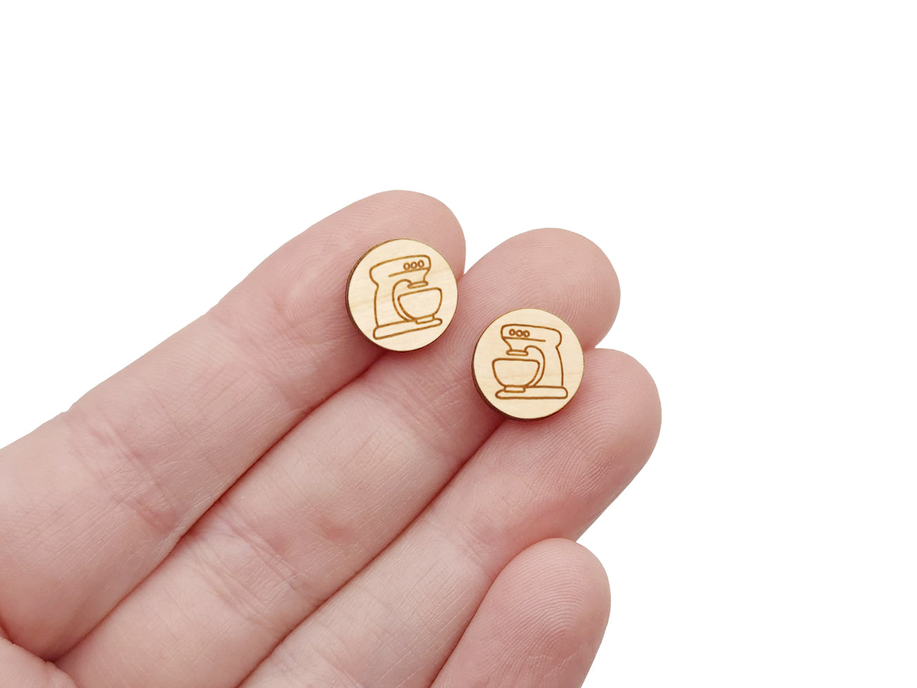 a hand holding a pair of round wooden cabochon earring blanks engraved with a kitchen mixer