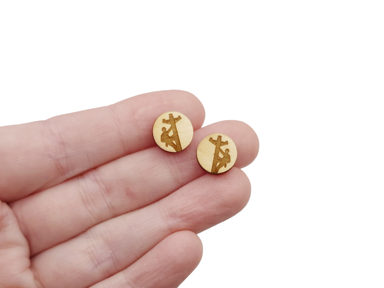 a person holding a pair of round wooden cabochon earring blanks engraved with a lineman