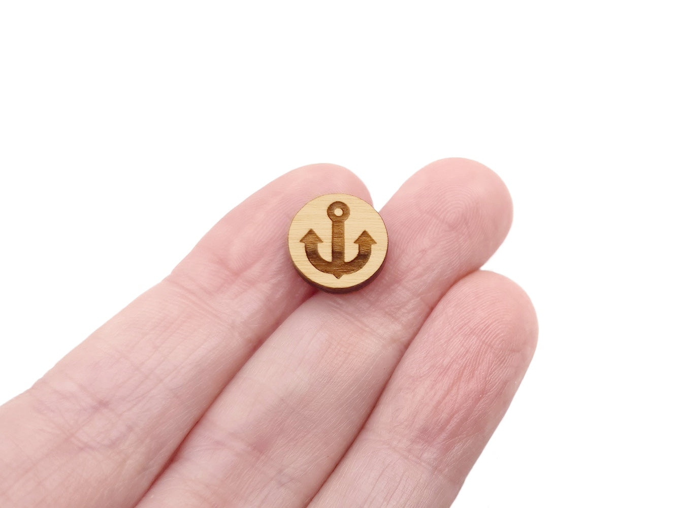 a hand holding a round wooden cabochon earring blank engraved with an anchor silhouette