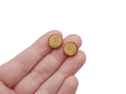 A hand holding a pair of wooden cabochon stud earring blanks cut and engraved to look like slices of wood